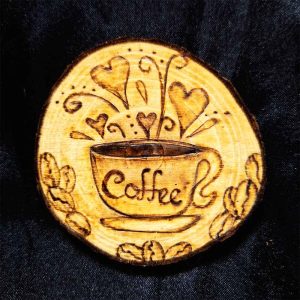 alt="3 inch by 3 inch hand burned round wood slice magnet with bark edge designed with a coffee cup on a saucer surrounded by hearts and coffee beans.">