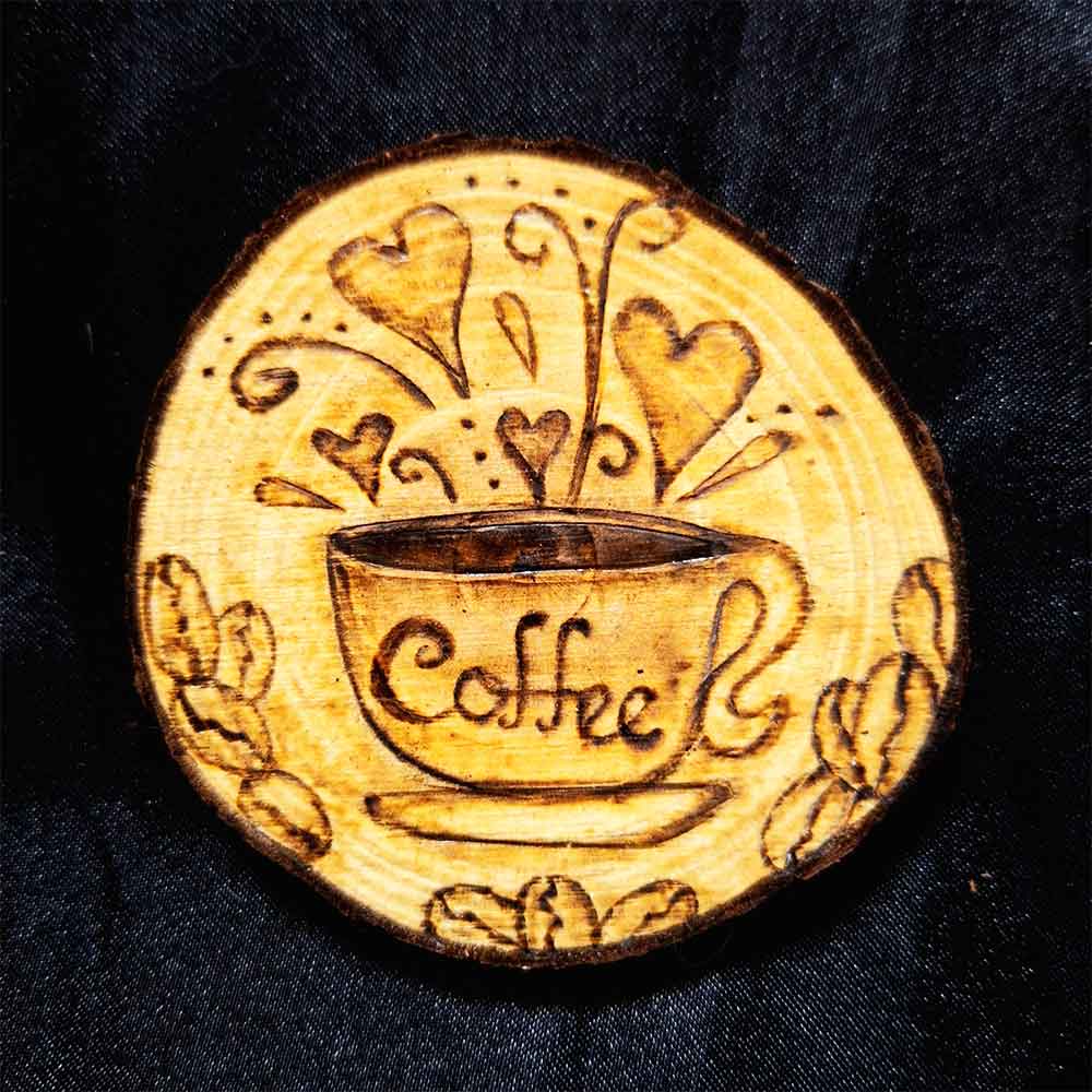 alt="3 inch by 3 inch hand burned round wood slice magnet with bark edge designed with a coffee cup on a saucer surrounded by hearts and coffee beans.">