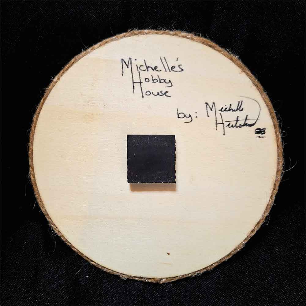 alt="View of the back artist and brand signatures on a 4 inch by 4 inch round wood slice magnet finished with a brown twine outer edge.">