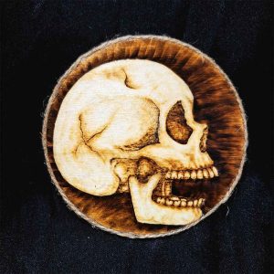 alt="4 inch by 4 inch round wood slice magnet designed with hand burned human skull art finished with a brown twine outer edge.">