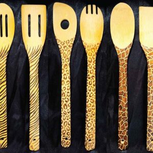 alt="Six side by side full size wooden kitchen utensils, spoon and spatula sets, designed with hand burned giraffe, zebra and leopard print fully wrapping the entire handle.">