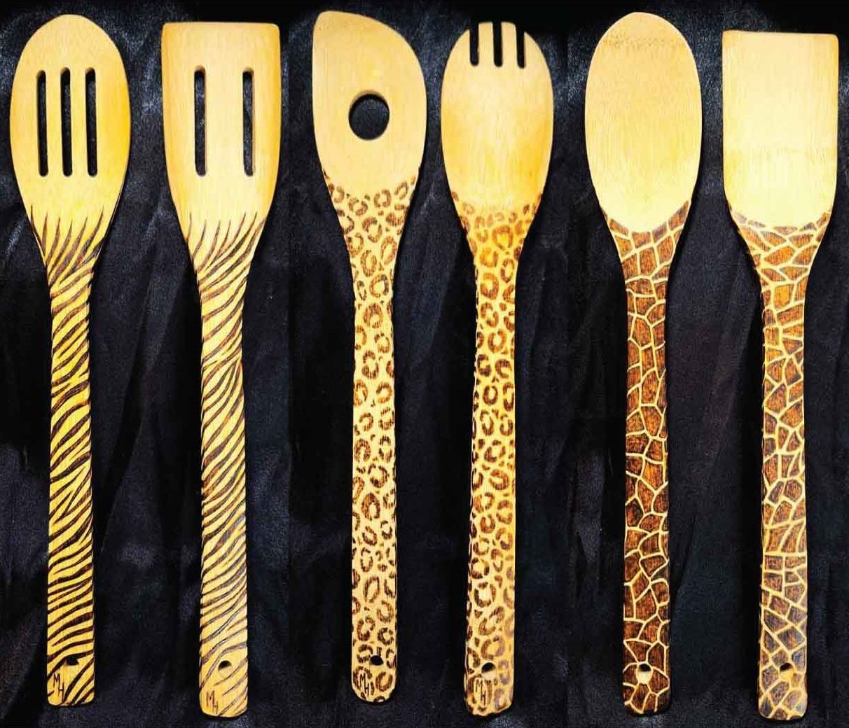 alt="Six side by side full size wooden kitchen utensils, spoon and spatula sets, designed with hand burned giraffe, zebra and leopard print fully wrapping the entire handle.">
