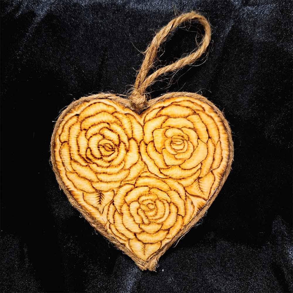 alt="3 inch by 3 inch heart shaped wood slice designed with 3 roses artwork hand burned finished with a brown twine outer edge with a loop for wall hanging.">