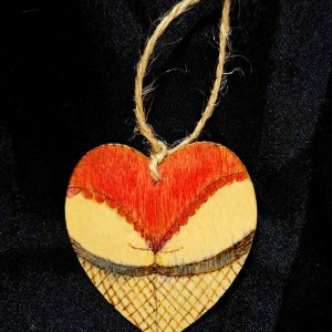 alt="Small 2 inch by 2 inch hand burned heart shaped wood slice designed with a woman's round butt cheeks in red colored lace panties and black colored fishnet stocking thighs in the shape of the heart finished with a brown twine loop for wall hanging.">