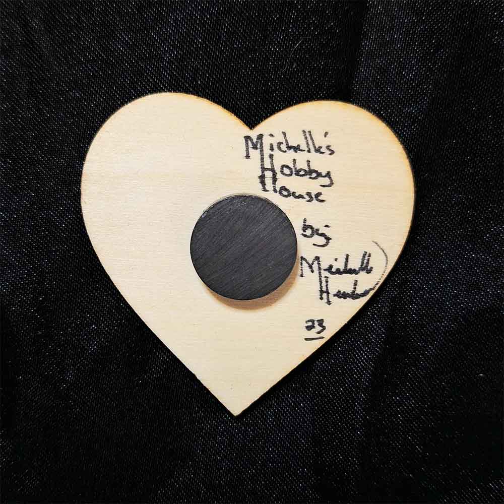 alt="View of the back artist and brand signatures on a small 2 inch by 2 inch hand burned heart shaped wood slice magnet.">