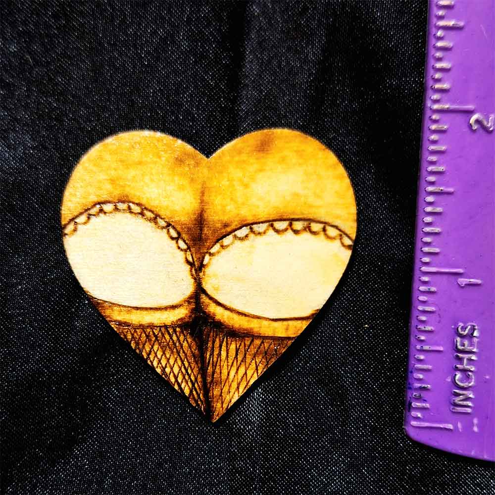 alt="Vertical ruler measuring a small 2 inch by 2 inch hand burned heart shaped wood slice magnet designed with a woman's round butt cheeks in lace panties and fishnet stocking thighs in the shape of the heart.">