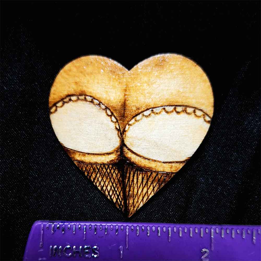 alt="Horizontal ruler measuring a small 2 inch by 2 inch hand burned heart shaped wood slice magnet designed with a woman's round butt cheeks in lace panties and fishnet stocking thighs in the shape of the heart.">