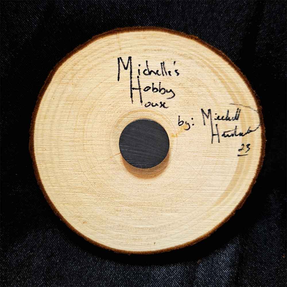 alt="View of the back artist and brand signatures on a 3 inch by 3 inch hand burned round wood slice magnet with bark edge.">
