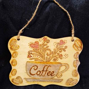 alt="3 inch by 4 inch hand burned rectangle slice with decorative shaped edge designed with a blue coffee cup on a saucer that says 'Coffee' with red hearts and brown decorative swirl splashes coming out of the top and brown coffee beans framing the left and right sides finished with a brown twine top loop for wall hanging display.">