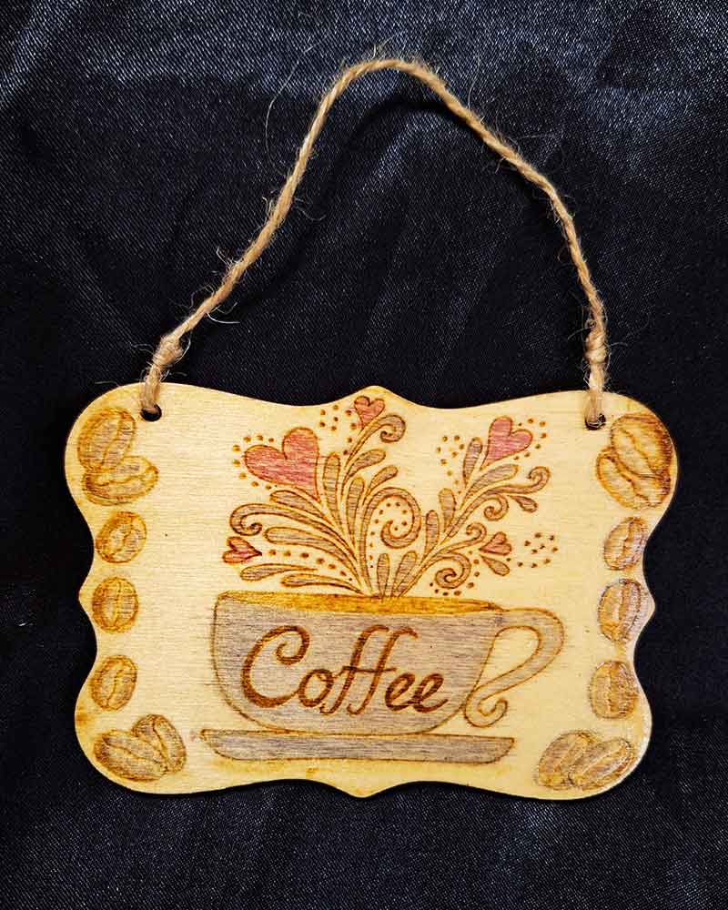 alt="3 inch by 4 inch hand burned rectangle slice with decorative shaped edge designed with a blue coffee cup on a saucer that says 'Coffee' with red hearts and brown decorative swirl splashes coming out of the top and brown coffee beans framing the left and right sides finished with a brown twine top loop for wall hanging display.">