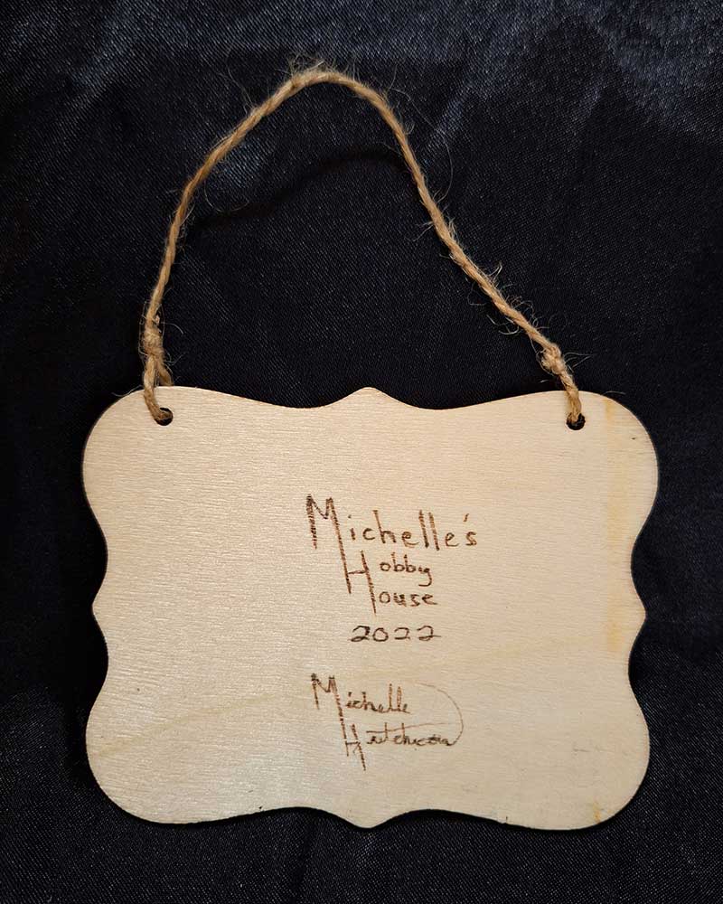 alt="View of the back artist and brand signatures on a 3 inch by 4 inch hand burned rectangle slice with decorative shaped edge finished with a brown twine top loop for wall hanging display.">