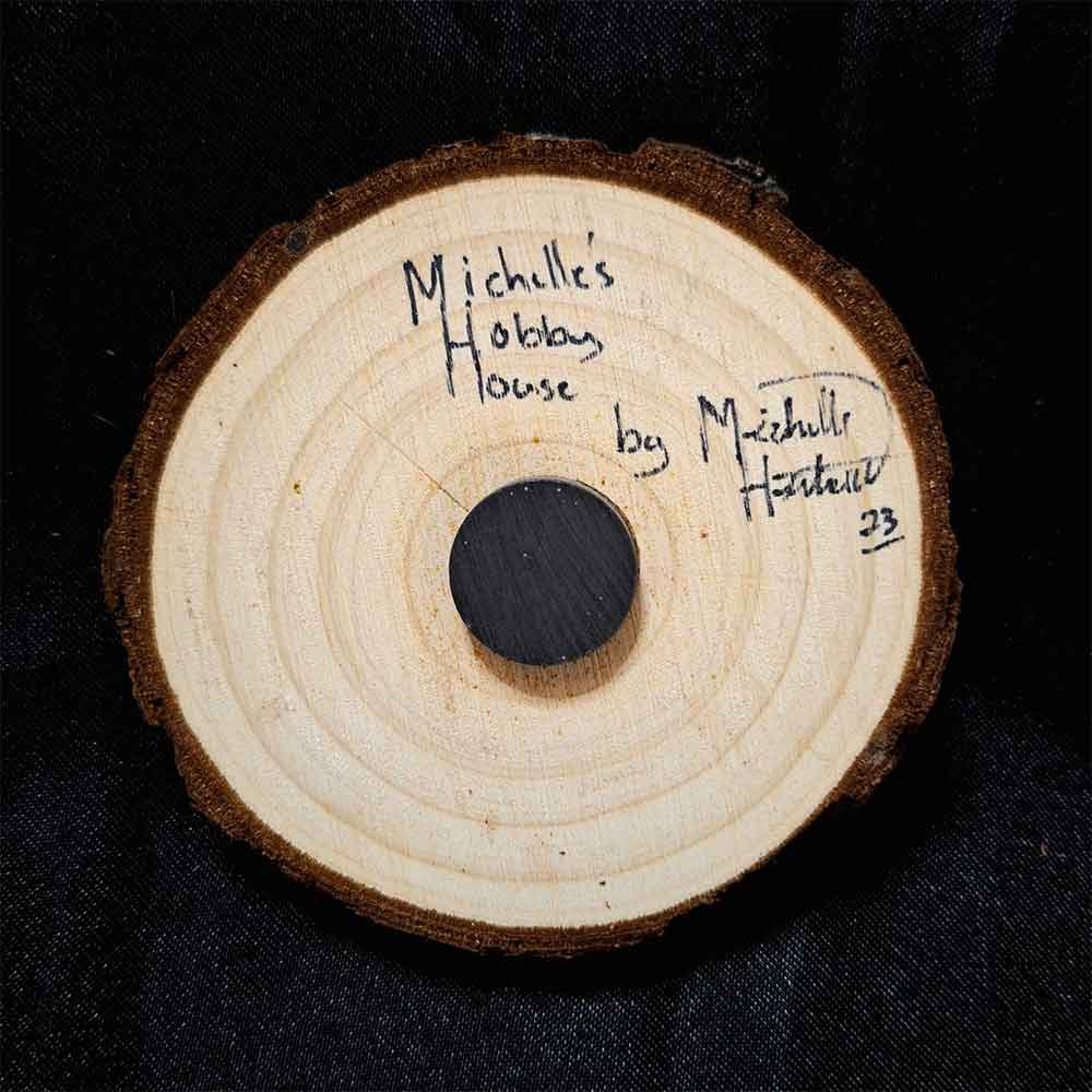 alt="View of the back artist and brand signatures on a 3 inch by 3 inch hand burned round wood slice magnet with bark edge.">