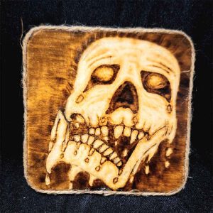 alt="4 inch by 4 inch square wood slice magnet designed with hand burned haunting melting zombie skull artwork finished with a brown twine outer edge.">