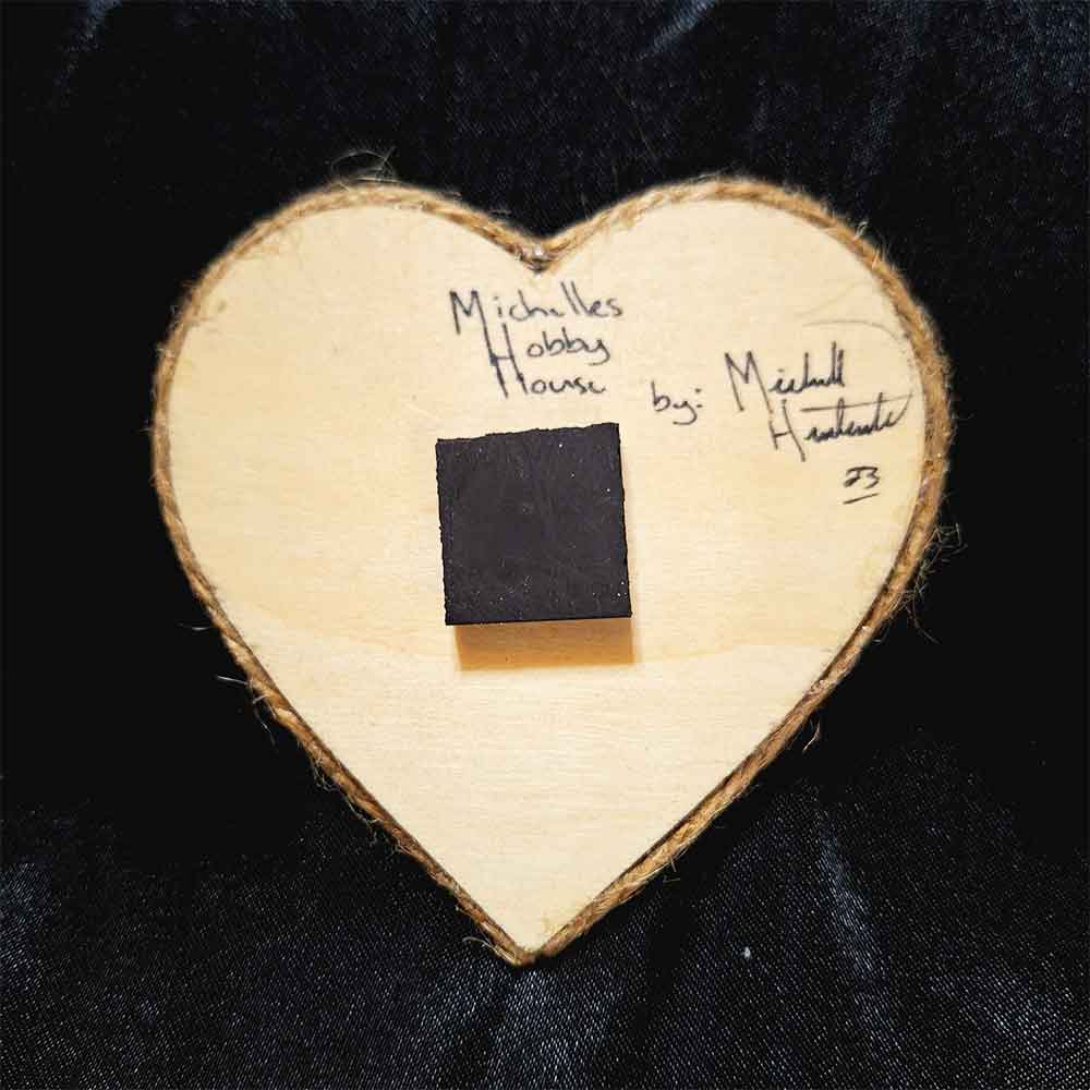 alt="View of the back artist and brand signatures on a 3 inch by 3 inch hand burned heart shaped wood slice finished with a brown twine edge border.">