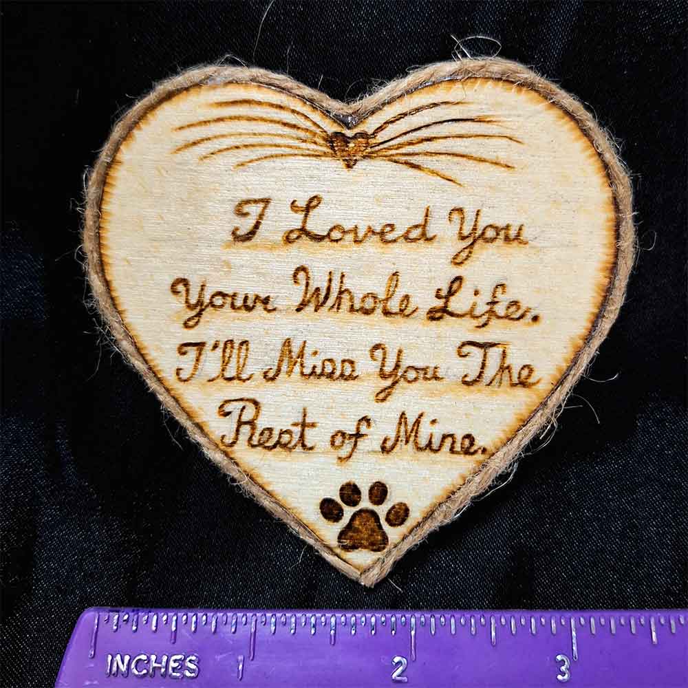 alt="Horizontal ruler measuring a 3 inch by 3 inch hand burned heart shaped wood slice magnet with pet nose and whisker art at the top and poem that says 'I loved you your whole life, I'll miss you the rest of mine,' finished with a brown twine edge border.">