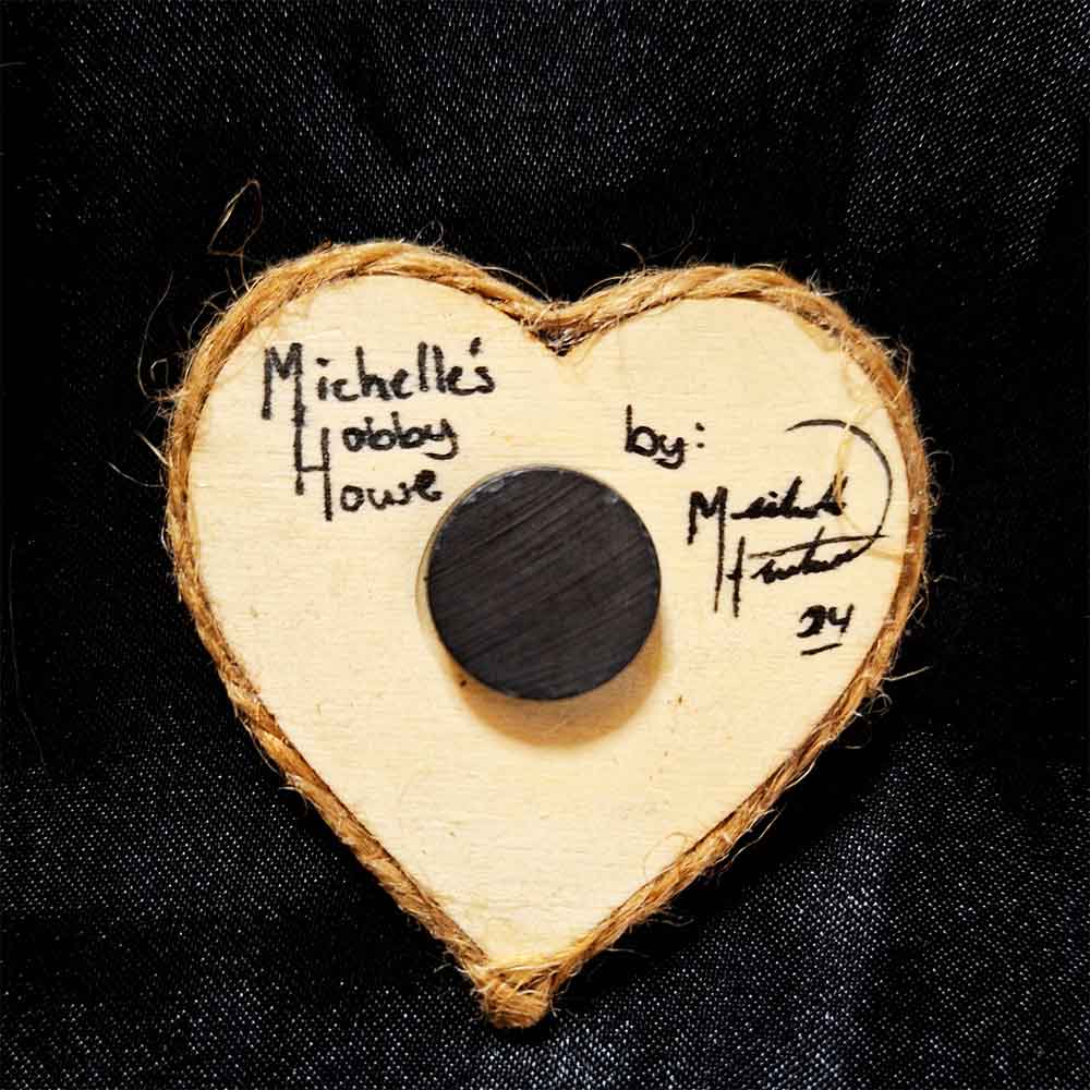 alt="View of the back artist and brand signatures on a small 2 inch by 2 inch hand burned heart shaped wood slice magnet finished with a brown twine edge border.">