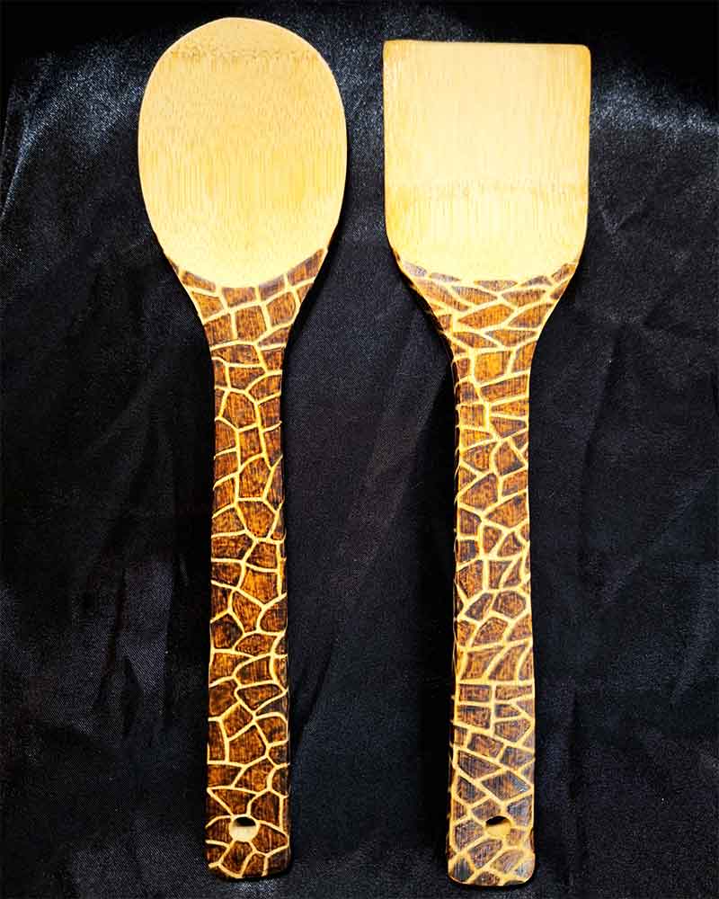 alt="Two side by side full size wooden kitchen utensils, one spoon and one spatula designed with hand burned giraffe print fully wrapping the entire handle.">