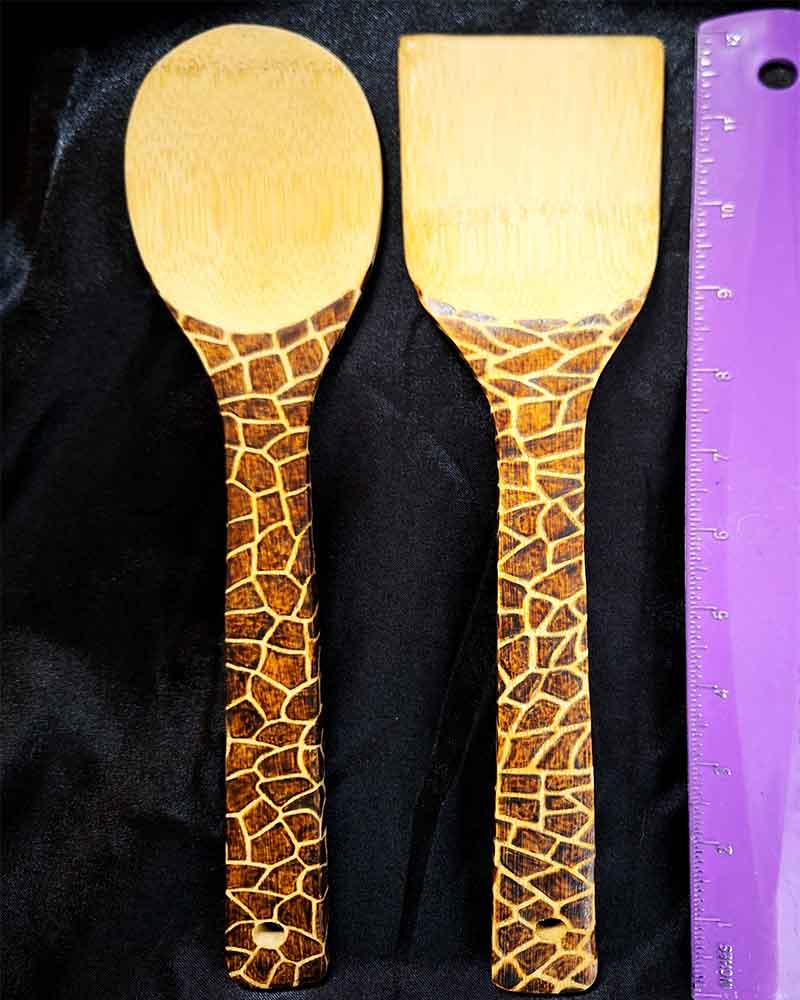 alt="Vertical ruler measuring two side by side full size wooden kitchen utensils, one spoon and one spatula designed with hand burned giraffe print fully wrapping the entire handle.">