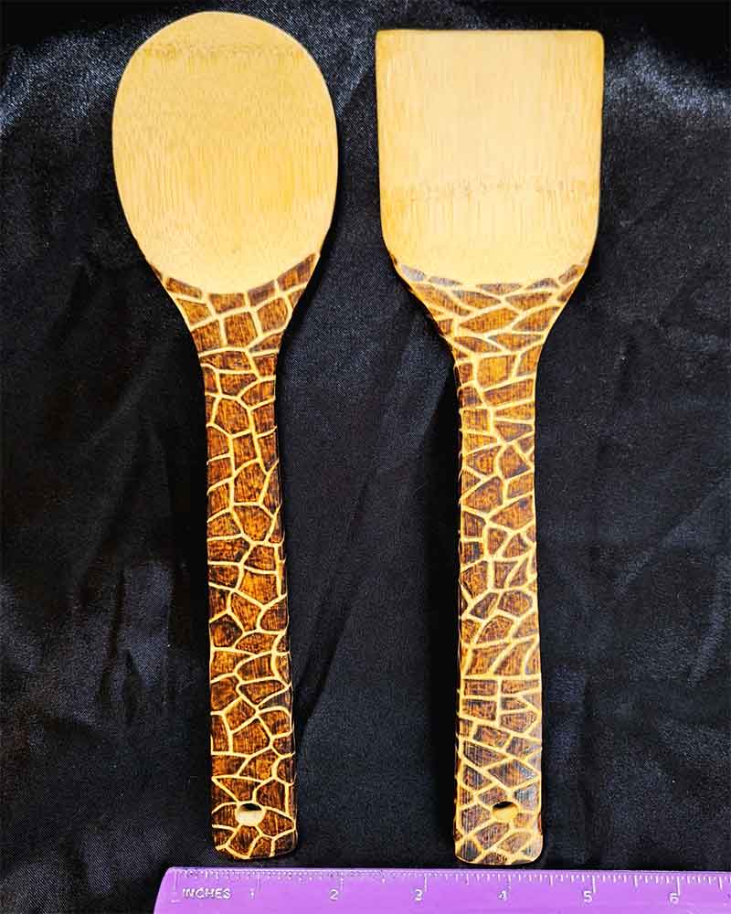 alt="Horizontal ruler measuring two side by side full size wooden kitchen utensils, one spoon and one spatula designed with hand burned giraffe print fully wrapping the entire handle.">