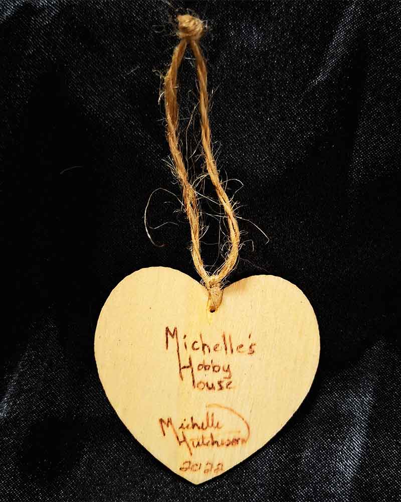 alt="View of the back signatures on a small 2 inch by 2 inch hand burned heart shaped wood slice finished with a brown loop for hanging on display.">