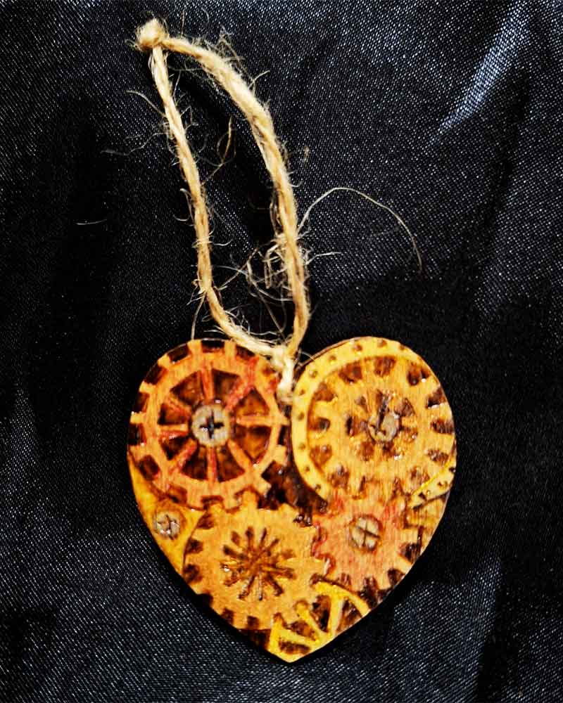alt="Small 2 inch by 2 inch hand burned heart shaped wood slice with steampunk art with metallic painted gears finished with a brown twine loop for wall hanging">