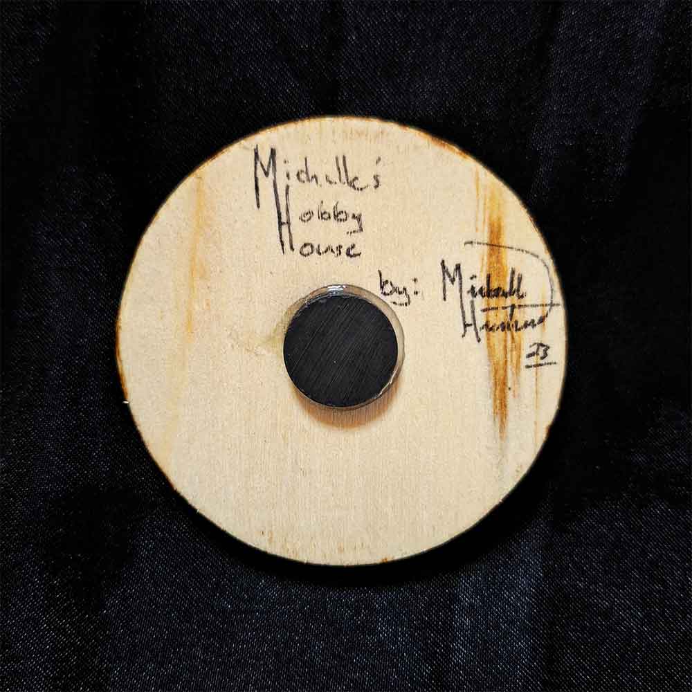 alt="View of the back artist and brand signatures on a 2.5 inch by 2.5 inch round wood slice magnet.">