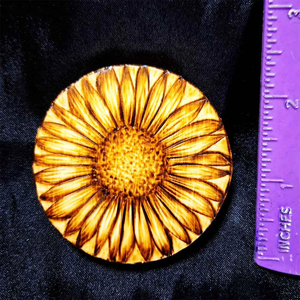 alt="Vertical ruler measuring a small 2.5 inch by 2.5 inch round wood slice magnet designed with hand burned sunflower artwork.">