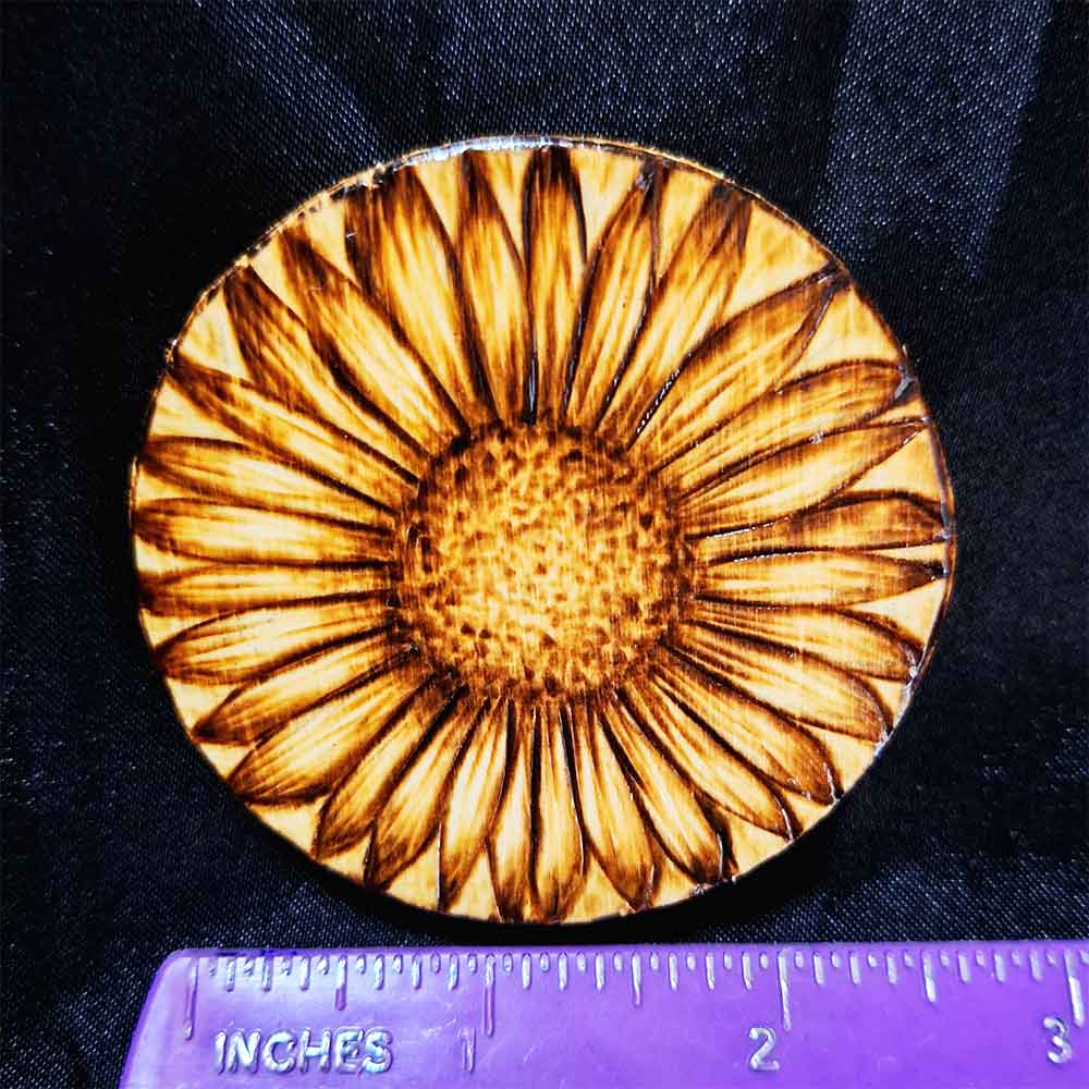 alt="Horizontal ruler measuring a small 2.5 inch by 2.5 inch round wood slice magnet designed with hand burned sunflower artwork.">